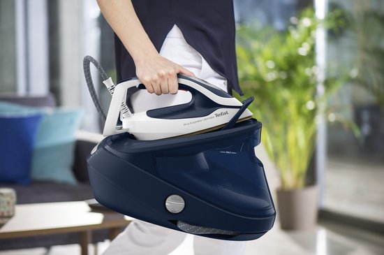 Een vrouw draagt de donkerblauwe Tefal Pro Express Ultimate II stoomgenerator, met het witte strijkijzer erin geplaatst.