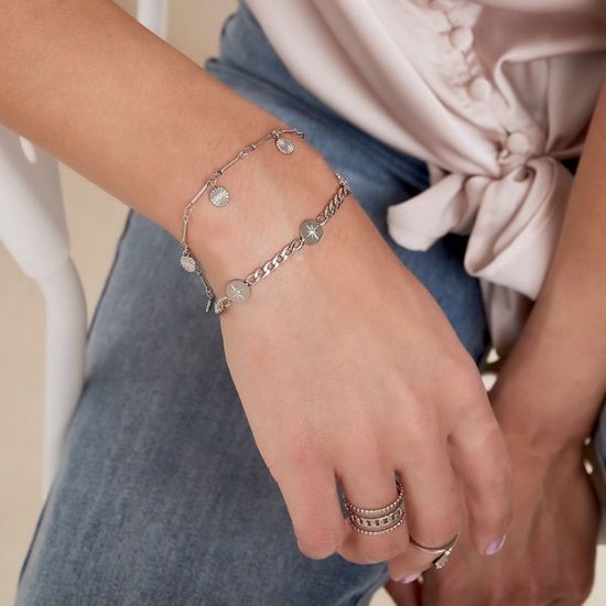 Zilverkleurige schakelarmband met drie ronde bedels en meerdere kleine disc-bedels. Gedragen op een arm met spijkerbroek en satijnen blouse.