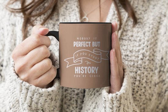 Tasse marron avec bordure et anse noires. Texte : "NOBODY IS PERFECT BUT IF YOU STUDY HISTORY YOU'RE CLOSE"
