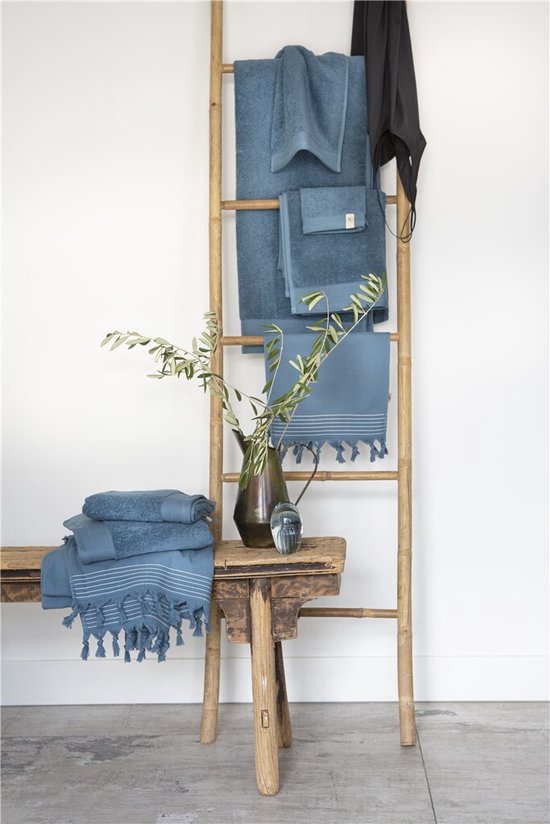Washandjes in petrolkleur met decoratieve franjes, op een ladder en bank.