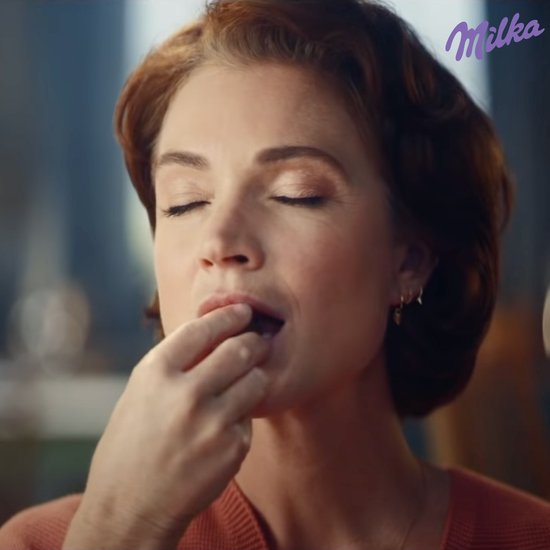 Een vrouw met ogen gesloten en een glimlach eet een stukje chocolade.