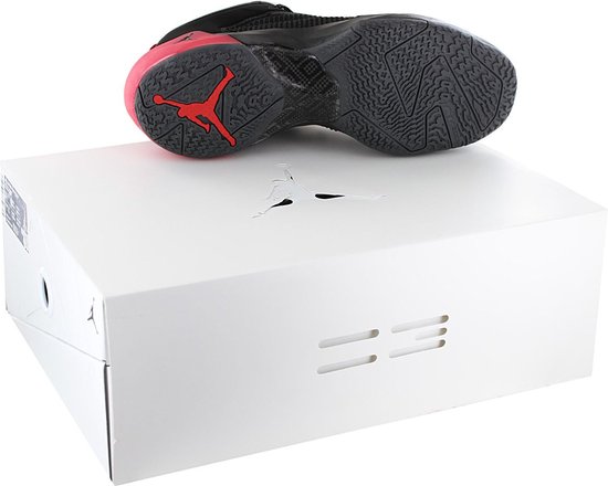 Onderkant van een zwarte Jordan basketbalschoen met rode zool en Jordan logo op een witte schoenendoos.