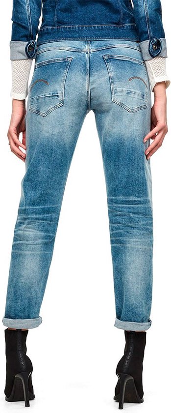 Gedragen achterkant van een vrouw in een lichte, gescheurde jeans met opgerolde broekspijpen en zwarte laarzen.