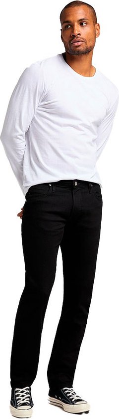 Man met witte longsleeve en zwarte jeans, staand.