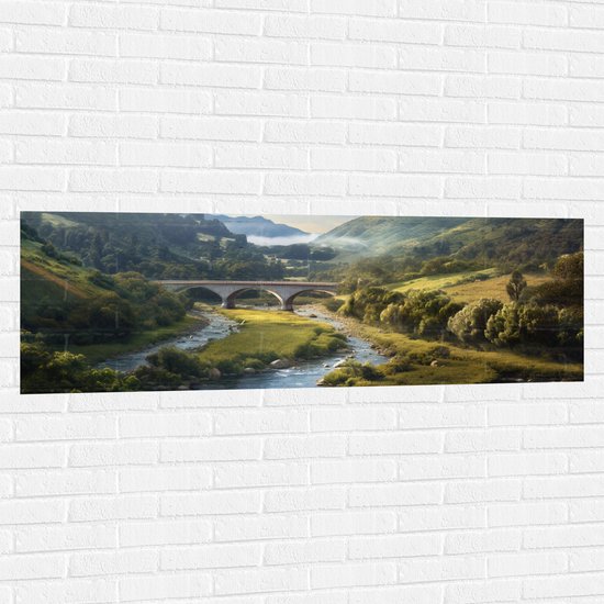 Muursticker - Rivier - Bergen - brug - Water - Stenen - Gras - Bomen - Wolken - 150x50 cm Foto op Muursticker