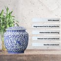 Blauw-witte porseleinen urn met bloemenpatroon, naast een bamboeplant en op houten plank.