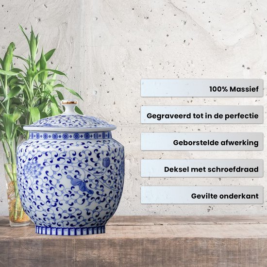 Blauw-witte porseleinen urn met bloemenpatroon, naast een bamboeplant en op houten plank.