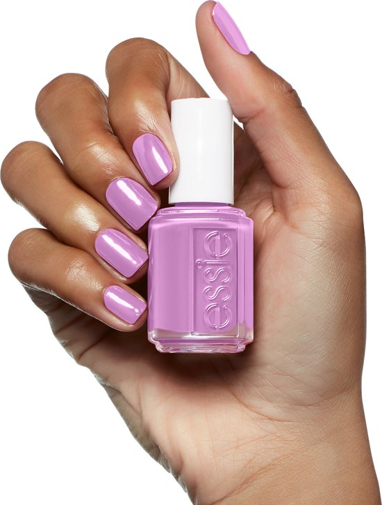 Hand met gelakte nagels in paars-roze, houdt een flesje Essie nagellak in dezelfde kleur vast.