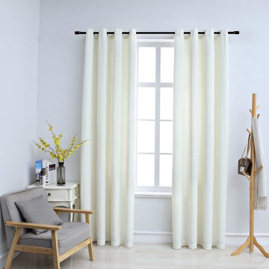 Twee gebroken witte fluwelen gordijnen hangen voor een raam in een woonkamer, naast een stoel en kapstok.