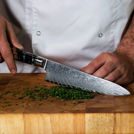 Een chef-kok snijdt bieslook met een Japans santokumes met damastpatroon en houten/epoxy handvat.