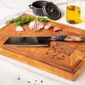 Een cleaver met blauwe epoxy en hout handvat, op een houten snijplank met knoflook, dille en peperkorrels.