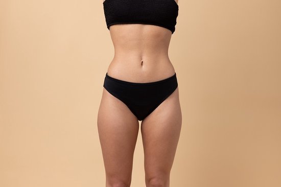 Devant d'une femme portant un bas de bikini noir taille basse sur fond beige.