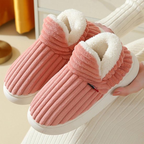 Roze corduroy winterslipper met dikke witte pluche voering, vastgehouden door een persoon.