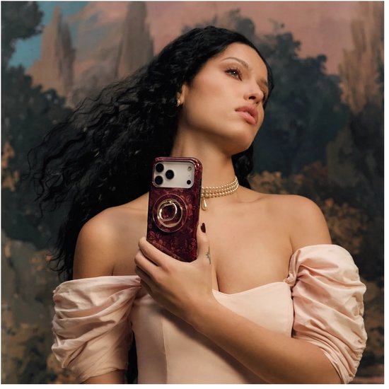 Vrouw in een roze jurk houdt een iPhone met een donkerrood bloemmotief hoesje en een goudkleurige ringhouder vast.
