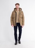Man draagt beige poloshirt met lange mouwen, beige jas, donkerblauwe broek en zwarte laarzen.
