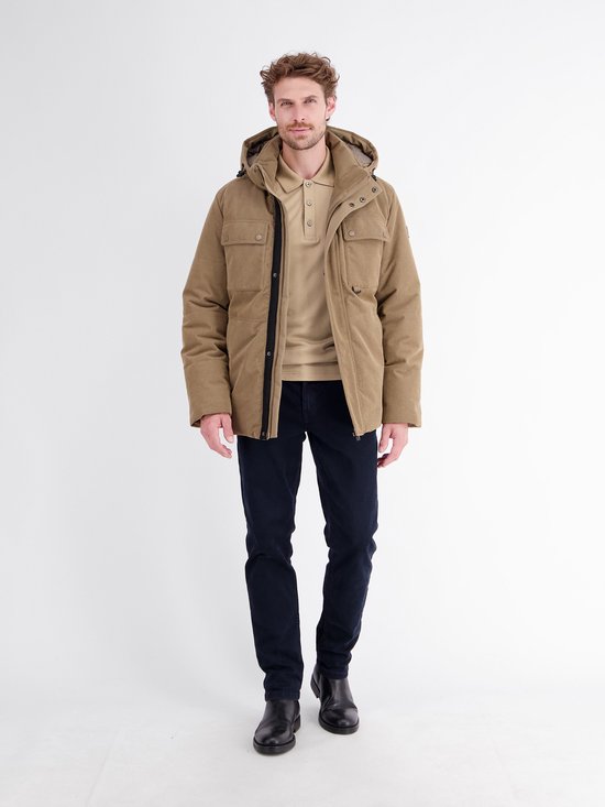Man draagt beige poloshirt met lange mouwen, beige jas, donkerblauwe broek en zwarte laarzen.