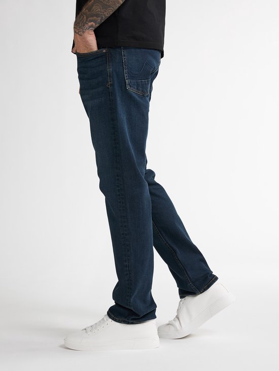 Man met een zwarte t-shirt en donkerblauwe denim jeans met rechte pasvorm. Hij draagt witte sneakers.