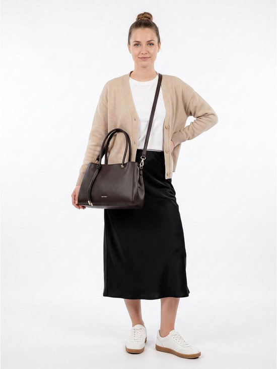 Vrouw met een beige vest en zwarte rok draagt een donkerbruine SURI FREY handtas.