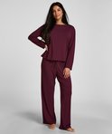 Vrouw in een paarse pyjamaset bestaande uit een top met lange mouwen en wijde broek.