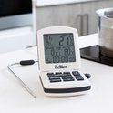 Witte ChefAlarm thermometer met roestvrijstalen sonde, staand op een aanrecht naast een pan.