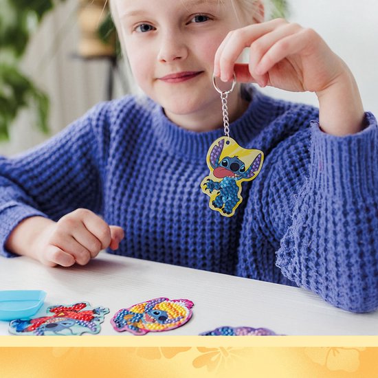 Kind in paarse trui houdt een Stitch-sleutelhanger vast bij een diamond painting-set op tafel.