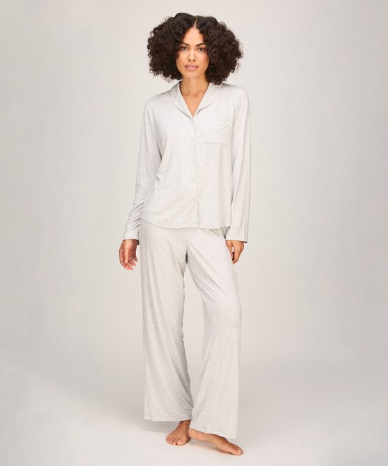 Model draagt een lichtgrijze pyjamaset bestaande uit een shirt met knoopsluiting en een bijpassende lange broek.