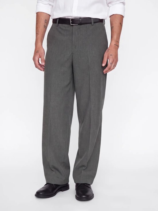 Man, voorste gedeelte, draagt grijze pantalon met wijde pijpen, witte overhemd, bruine riem en zwarte schoenen. Getatoeëerde armen.