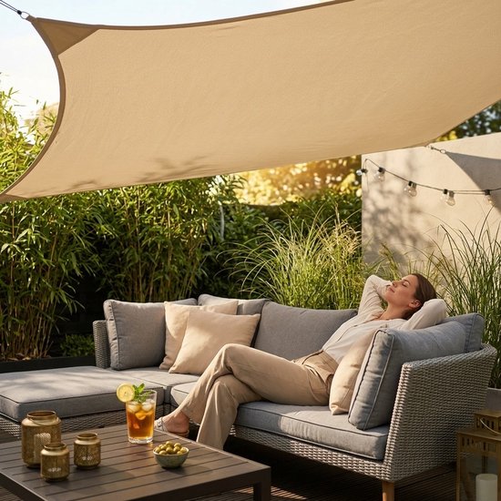 Vrouw ontspant op een grijze loungebank onder een beige vierkant schaduwdoek in de tuin.