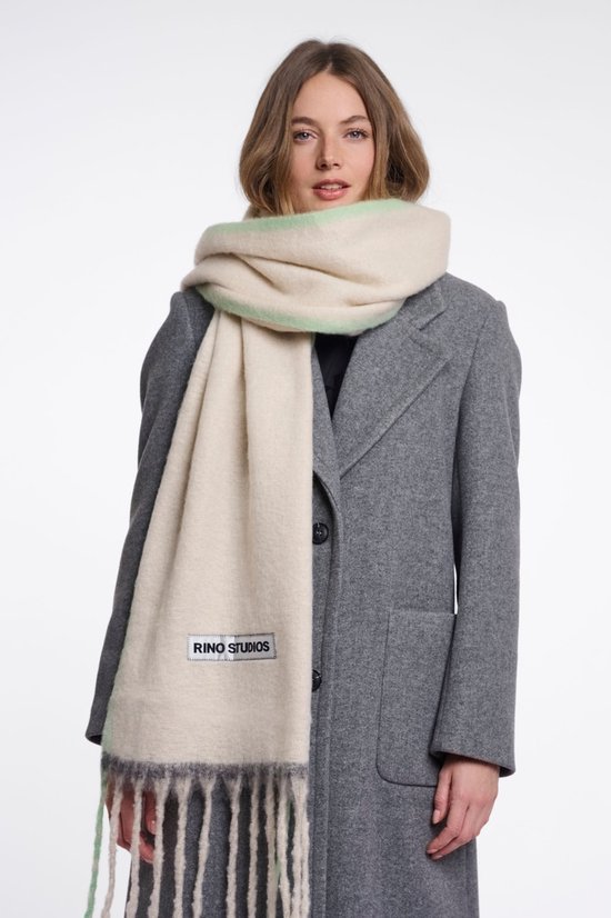 Beige sjaal met lichte mintgroene rand en franjes, met een Rino Studios label. Gedragen door een vrouw met grijs jasje.