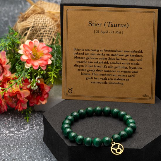 Armband van groene malachietkralen met een gouden Stier-bedel op een kaart met sterrenbeeldinformatie.