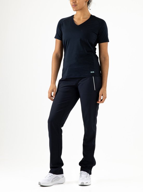 Model in een donkerblauwe V-hals sportshirt en bijpassende trainingsbroek met witte sneakers.