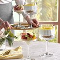 Drie dessertglazen op een tafel, twee gevuld met fruit en één met een witte dessertlaag en citroen, naast een vaas met bloemen.