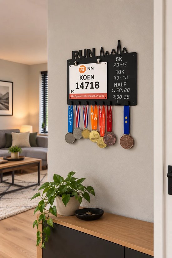 Zwarte metalen medaillehouder met 'RUN' silhouet, startnummerklem en krijtbord voor tijdsregistratie aan een wand.