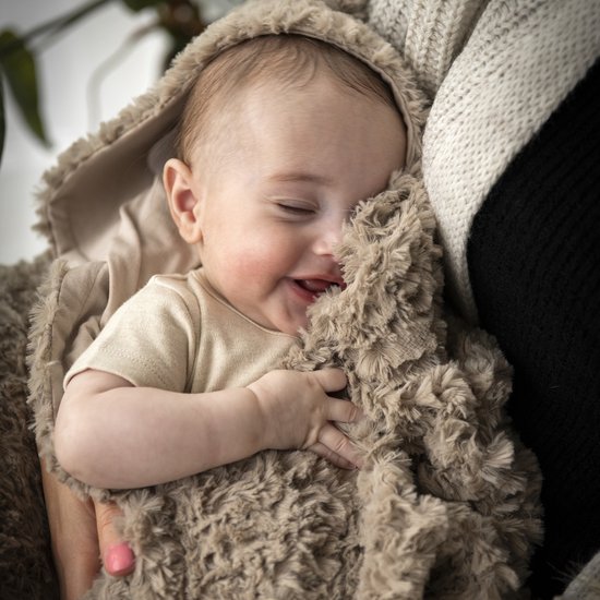 Un bébé souriant dans une couverture enveloppante marron avec des oreilles d'ours.