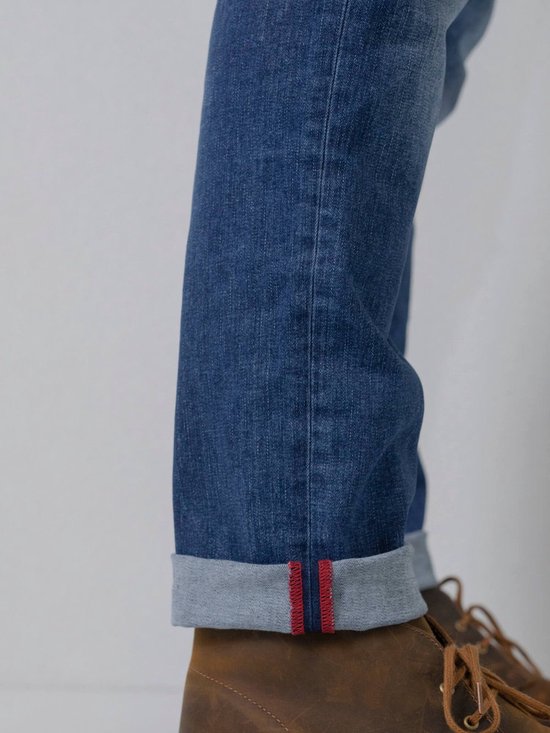 Pijp van een donkerblauwe jeans met opgerolde zoom en rode stiksels.