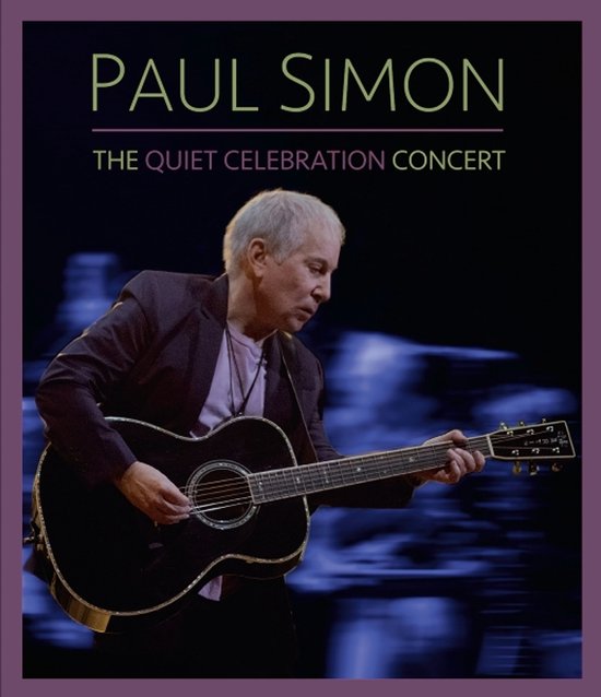Paul Simon speelt op een zwarte akoestische gitaar tijdens The Quiet Celebration Concert tegen een donkere achtergrond.