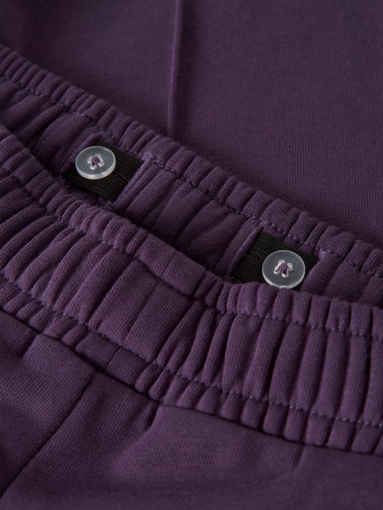 Detailopname van de verstelbare tailleband met elastiek en knoopjes aan de binnenzijde van de paarse joggingbroek.