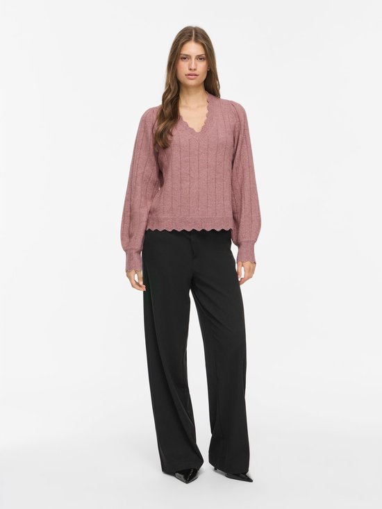 Model draagt een roze VILA gebreide trui met V-hals, geschulpte randen en zwarte pantalon.