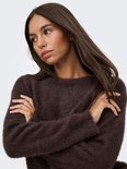 Model draagt een donkerbruine, harige trui met lange mouwen en ronde hals, armen over elkaar.