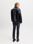 Achteraanzicht van een model in een grijze slim fit jeans en zwarte leren jas.