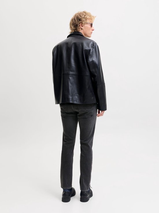 Achteraanzicht van een model in een grijze slim fit jeans en zwarte leren jas.