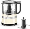 Gebroken witte KitchenAid hakmolen met een transparante kom, zwarte deksel en mes, met een extra mes naast de machine.