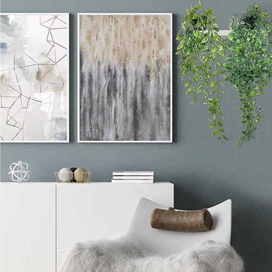 Groene kunstplanten hangend aan een muur naast moderne schilderijen, boven een witte kast.