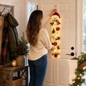 Vrouw hangt een sneeuwpop kersthanger aan een witte deur in een hal met warme sfeerverlichting.