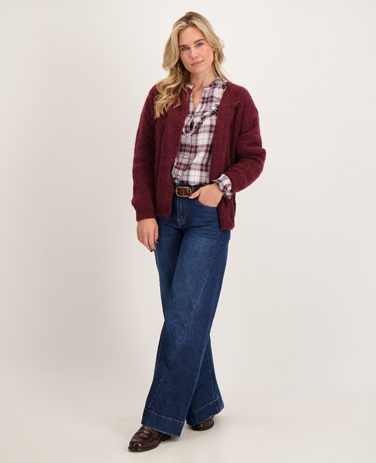 Model draagt een bordeauxrood vest over een geruite blouse en een donkerblauwe wide-leg jeans.