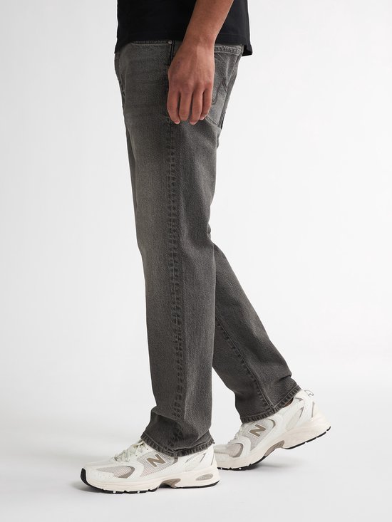 Een man draagt een grijze, rechte spijkerbroek van Petrol Industries. De broek heeft een casual uitstraling met zichtbare naden.
