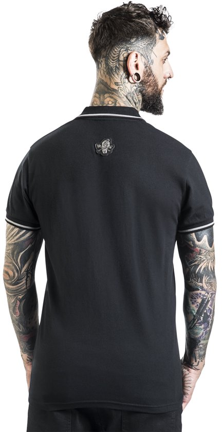 Zicht op de achterkant van een man met tatoeages die een zwart poloshirt draagt met witte biezen en een patch op de rug.