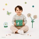 Een lachende jongen in gestreepte trui en corduroy broek, zittend met een doosje 'a butterfly garden for you'.