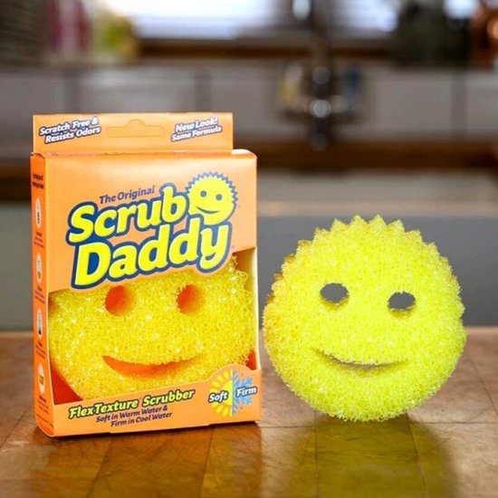 Gele Scrub Daddy spons met lachende gezichtjes, naast de verpakking.