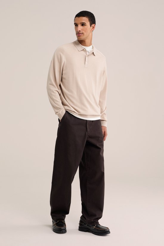 Man in beige coltrui, wit t-shirt, bruine chino en bruine loafers.